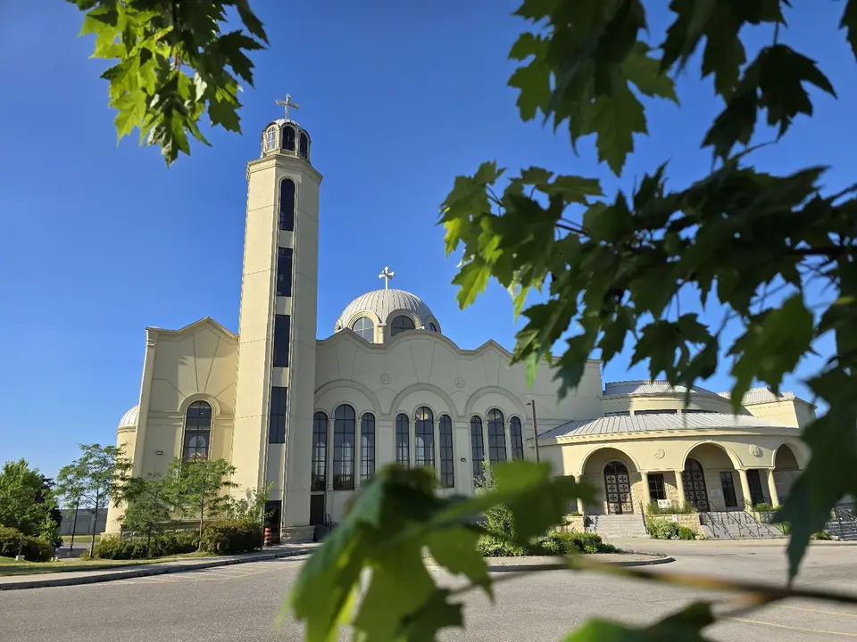 The bell tower and dome of Saint Mary and Saint Abraam under a clear blue sky, framed by maple leaves